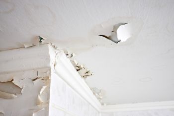 Peeling ceiling paint and water damage in a room corner near a window trim