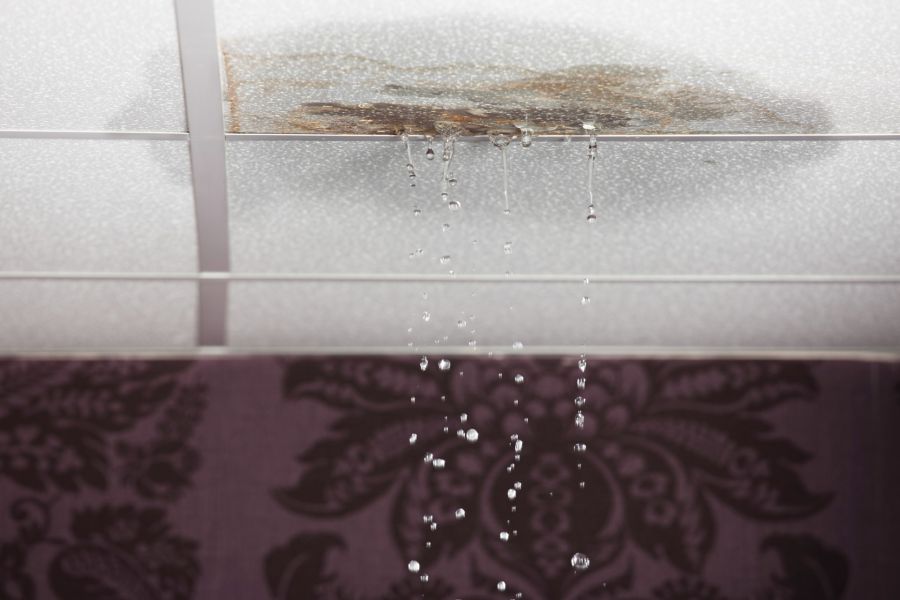 Water dripping from a stained ceiling tile, showing an active roof leak indoors